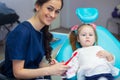 Pediatric dentist educating a smiling little girl about proper tooth-brushing, demonstrating on a model. Early