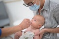 Pediatrician administring oral vaccination against rotavirus infection to little baby in presence of his mother