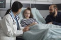 Pediatrician discussing with sick little daughter resting in patient bed