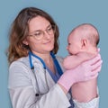 Pediatrician doctor holding newborn baby and smiling, blue studio background. Happy nurse in uniform with a baby in her arms Royalty Free Stock Photo