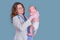 Pediatrician doctor holding newborn baby and smiling, blue studio background. Happy nurse in uniform with a baby in her arms Royalty Free Stock Photo