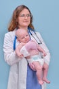 Pediatrician doctor holding newborn baby and smiling, blue studio background. Happy nurse in uniform with a baby in her arms Royalty Free Stock Photo