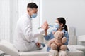 Pediatrician giving high five to girl in hospital. Doctor and patient wearing protective masks Royalty Free Stock Photo