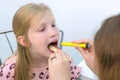 Pediatrician looking child girl sore throat using spatula and lantern.