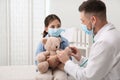 Pediatrician playing with girl during visit in hospital. Doctor and patient wearing protective masks Royalty Free Stock Photo
