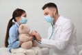 Pediatrician playing with girl during visit in hospital. Doctor and patient wearing protective masks Royalty Free Stock Photo