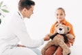 Pediatrist in white coat and kid with teddy bear in clinic