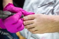 Pedicurist master in pink gloves cuts the cuticle and shellac toe nails in the pedicure salon using drill. Professional pedicure