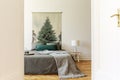 A peek through an open door into a simple style bedroom interior with a bed dressed in gray and green sheets, pillows and a wool b