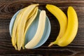 Peel of banana and peeled banana in blue plate, bunch of banana on wooden table. Top view