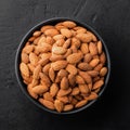 Peeled almonds in a bowl on a black textured background