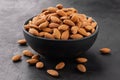 Peeled almonds in a bowl and a few nuts scattered around on a black textured background