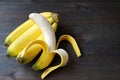 Peeled banana on a bunch of bananas isolated on dark brown wooden table Royalty Free Stock Photo