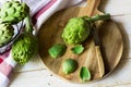 Peeled fresh artichoke preparing for cooking, wood cutting board, knife, vegetables in metal basket, rustic kitchen interior