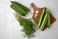 Peeled fresh cucumbers on a brown wooden cutting board with a bunch of dill and garlic on a light gray concrete table Royalty Free Stock Photo