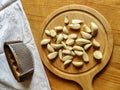 Peeled garlic cloves on chopping board, next to garlic chopper and gray linen towel on old wooden background. Concept of cooking Royalty Free Stock Photo