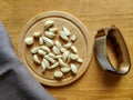 Peeled garlic cloves on chopping board, next to garlic chopper (press) and brown linen towel on old wooden background. Royalty Free Stock Photo