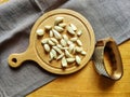 Peeled garlic cloves on chopping board, next to garlic chopper (press) and brown linen towel on old wooden background. Royalty Free Stock Photo