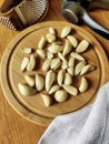 Peeled garlic cloves on chopping board, next to garlic choppers and gray linen towel on old wooden background. Concept of cooking Royalty Free Stock Photo