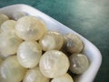 Peeled longan in a white square bowl on a green background. Royalty Free Stock Photo