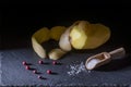 A peeled potato with the skin resting on top, red berries and a wooden spoon full of grains of salt on a slate plate