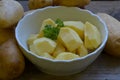 Peeled potatoes with parsley in white bowl on wooden background