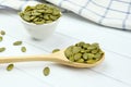 Peeled raw pumpkin seeds on a wooden spoon and in small ceramic bowl