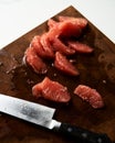 Peeled and sliced, divided in sections grapefruit on a wooden board with a knife next to it. The board rests on the