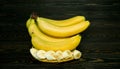 Peeled and sliced into pieces bright yellow juicy ripe banana and bundle of whole bananas on a coarse dark wooden background from Royalty Free Stock Photo