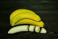 Peeled and sliced into pieces bright yellow juicy ripe banana and bundle of whole bananas on a coarse dark wooden background from