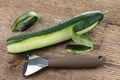 Peeler for cleaning vegetables and fruits with cucumber with peeled skin on a background of rough wooden