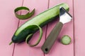 Peeler for cleaning vegetables and fruits with cucumber with peeled skin on a pink