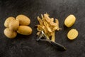 Peeler with peeled potatoes and their skins on textured black background