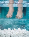 Peeling with fish and white spa stones. Girl enjoying medicinal procedure and receiving massage with small fishes. Foot massage Royalty Free Stock Photo