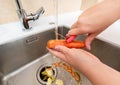 Peeling a fresh carrot under running water with waste collected in a garbage disposer. Royalty Free Stock Photo