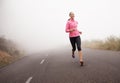 Peeling off the miles. a young woman jogging on a country road on a misty morning. Royalty Free Stock Photo