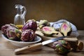 Small artichokes with olive oil, knife and cutting board on wooden background.