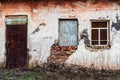 The peeling wall of an old abandoned building with closed doors and two windows close-up Royalty Free Stock Photo