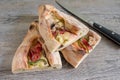 Peinirli - Greek open faced pizza with ham, cheese and vegetables, three half pieces on wooden kitchen surface with knife