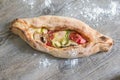 Peinirli - Greek open faced pizza with ham, cheese and vegetables just baked on wooden kitchen surface