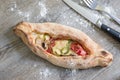 Peinirli - Greek open faced pizza just baked on wooden kitchen surface. Knife and fork on the side