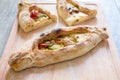 Peinirli - Greek open faced pizzas with ham, cheese and vegetables on wood cutting board