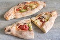 Peinirli - Greek open faced pizzas with ham, cheese and vegetables, one whole and one cut in half on wooden kitchen surface