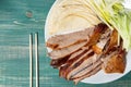 Peking Duck - Chinese roast duck with cucumber, onions and pancakes on wooden green table with chopsticks. Top view