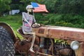 A skeleton, next to an American flag, sits in the driver seat of an old rusty tractor