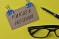 Pen, eyeglasses and brown card with text POLICIES & PROCEDURE