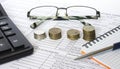 Pen on financial and accounting reports with coins stacks, glasses and calculator in background.