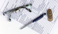 Pen on financial and accounting reports with coins stacks, glasses and calculator in background