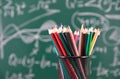 A pen holder filled with colored pencils in front of a blackboard full of mathematical formulas