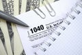 The pen, notebook and dollar bills is lies on the tax form 1040